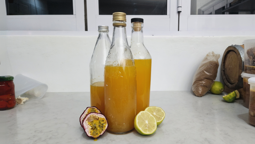 Bottles of homemade granadilla cordial on a kitchen counter, with fresh passionfruit and sliced lemon in the foreground.